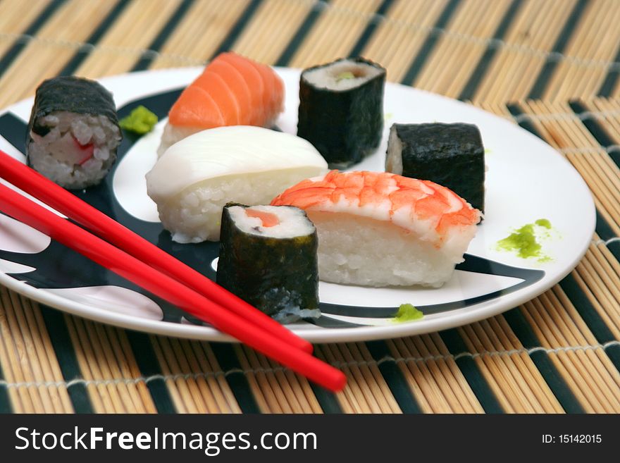 Assortment of sushi on a plate with red chopsticks on a circular decorated plate, on a wood table-cloth. Assortment of sushi on a plate with red chopsticks on a circular decorated plate, on a wood table-cloth