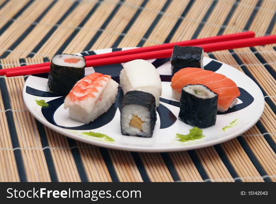 Assortment of sushi on a plate with red chopsticks and wasabi in a circular decorated plate, on a wood table-cloth. Assortment of sushi on a plate with red chopsticks and wasabi in a circular decorated plate, on a wood table-cloth