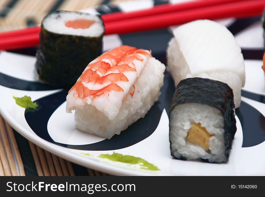 Assortment of sushi on a plate with red chopsticks on a circular decorated plate, on a wood table-cloth, close-up. Assortment of sushi on a plate with red chopsticks on a circular decorated plate, on a wood table-cloth, close-up
