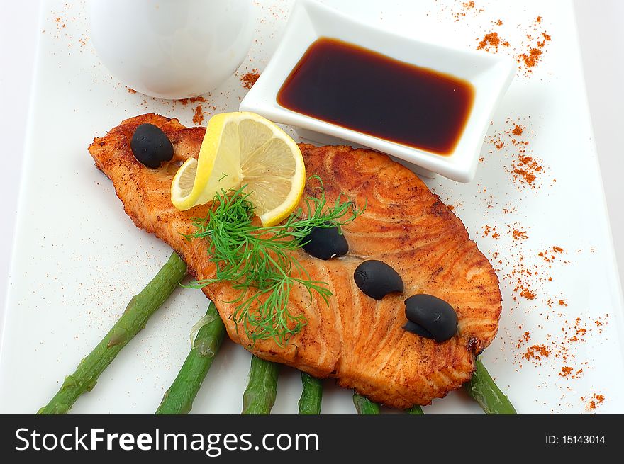 Salmon fried with spices with a lemon on a white plate with fennel