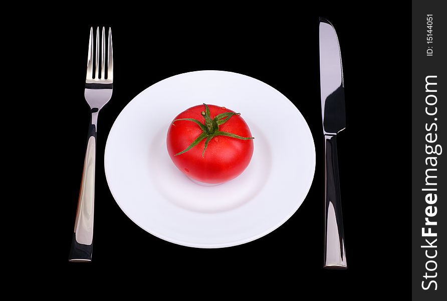 The knife, fork and fresh tomato on white plate. Black background. Isolated object
