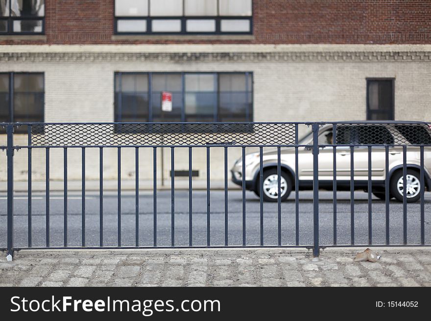 Iron fence on a city street with a building and a car driving in the background