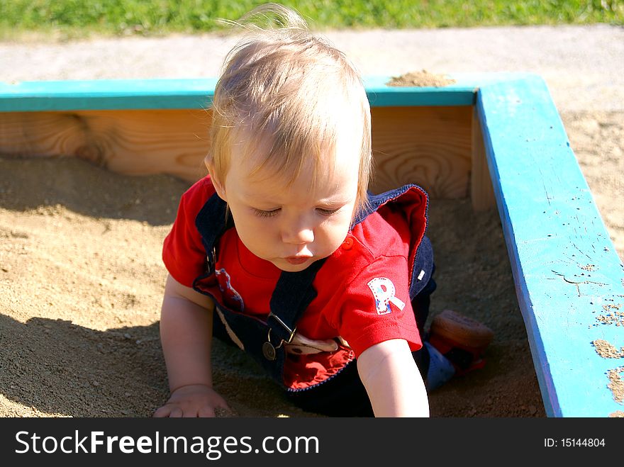 The small boy in clothes sits and plays in the summer in a sandbox. The small boy in clothes sits and plays in the summer in a sandbox
