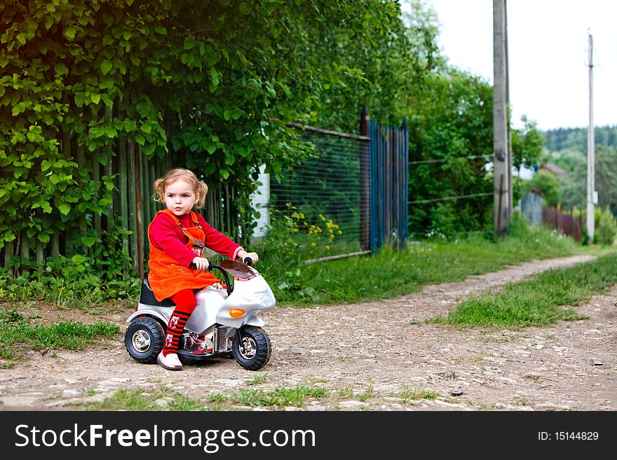 Portrait of little girl on toy moped looking aside. Portrait of little girl on toy moped looking aside