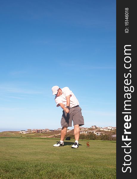 Young male golfer hitting the ball from the tee box next to the ocean on a beautiful summer day. Young male golfer hitting the ball from the tee box next to the ocean on a beautiful summer day