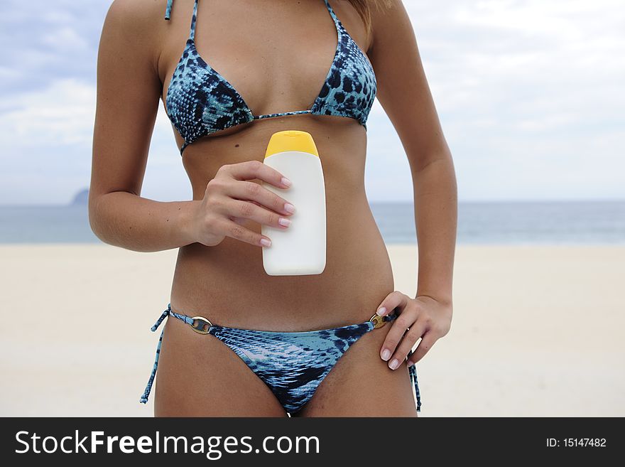 Woman in bikini holding suncream at the beach