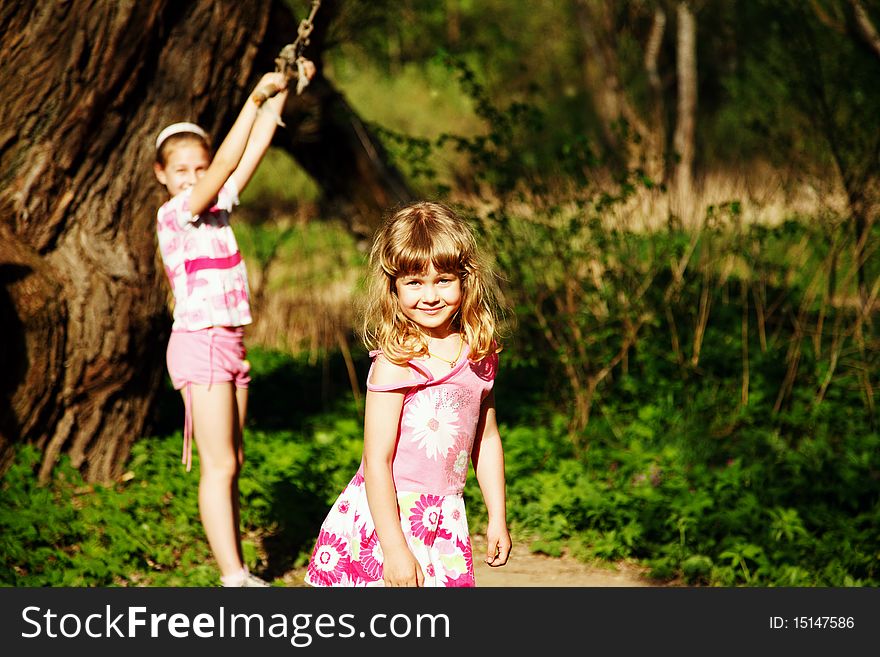 Two sisters near thick tree. One girl is holding swing and another just looking forward. Two sisters near thick tree. One girl is holding swing and another just looking forward