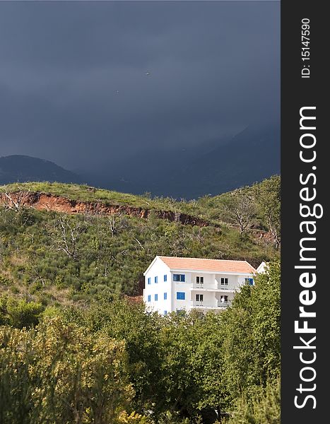 View of alone white building on the hillside at the foot of the mountains on the background of stormy skies near the town of Budva, Montenegro. View of alone white building on the hillside at the foot of the mountains on the background of stormy skies near the town of Budva, Montenegro