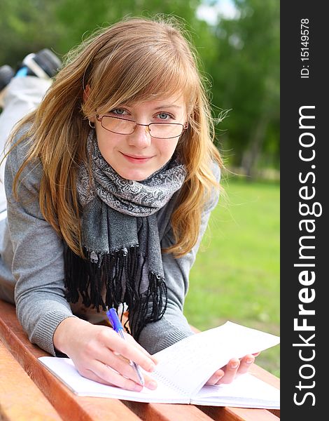 The girl lay on a bench, and writes. Outdoors