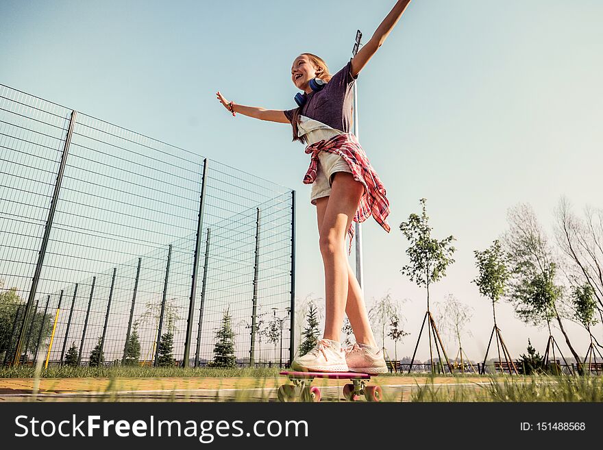 Beaming teenage girl actively riding on a skateboard and spreading her hands