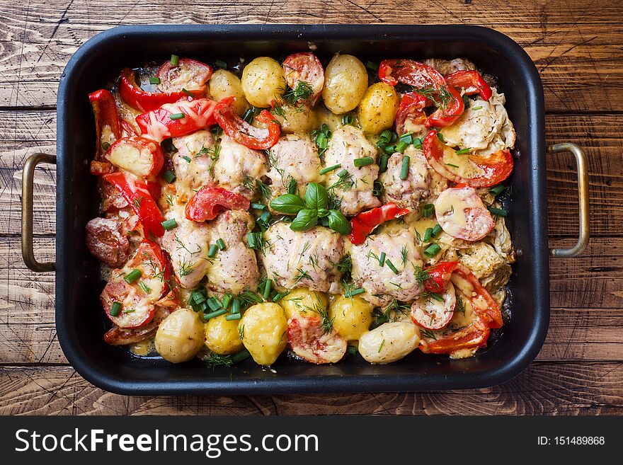 Baked chicken thighs, potatoes and vegetables in a baking tray on a wooden table