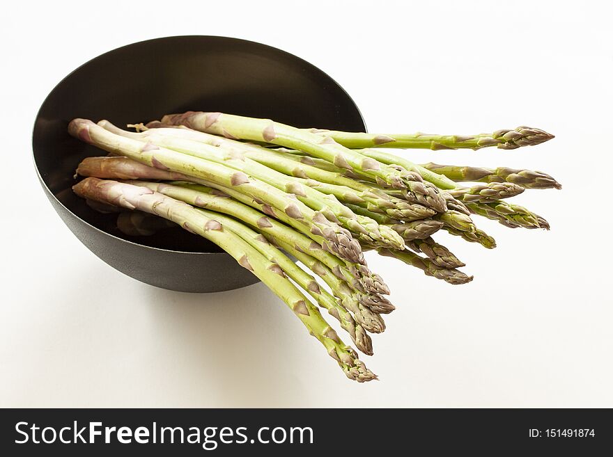 Bundle of green asparagus in a round black bowl. Close up image