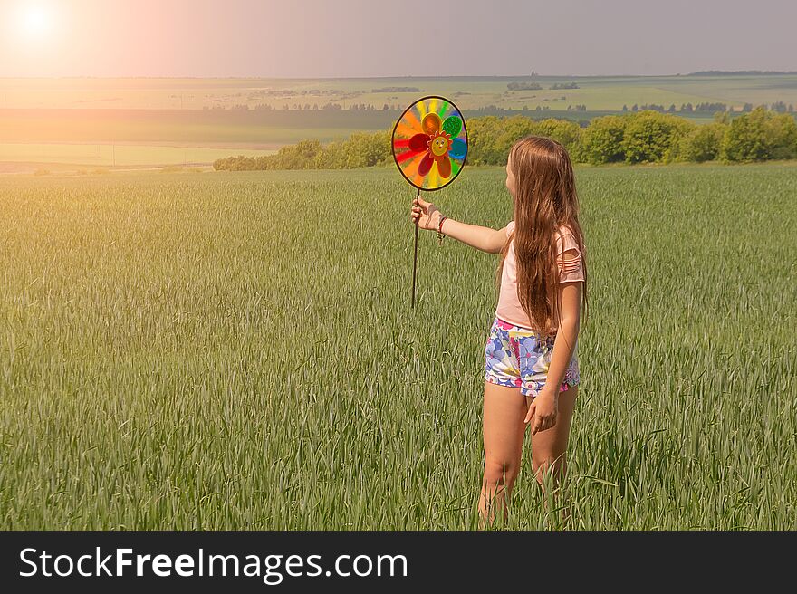 A happy girl with long hair is holding a colored windmill toy in her hands