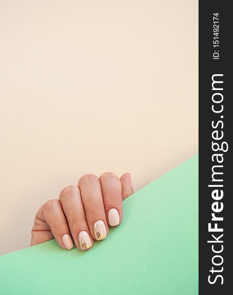 Young woman`s hand with beautiful manicure on beige and turquoise background with copyspace. Vertical picture. Young woman`s hand with beautiful manicure on beige and turquoise background with copyspace. Vertical picture