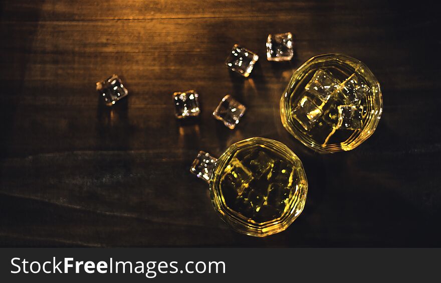 Top view whiskey in glass with beautiful amber ice, placed on a wooden table with a rough surface against a dark background and