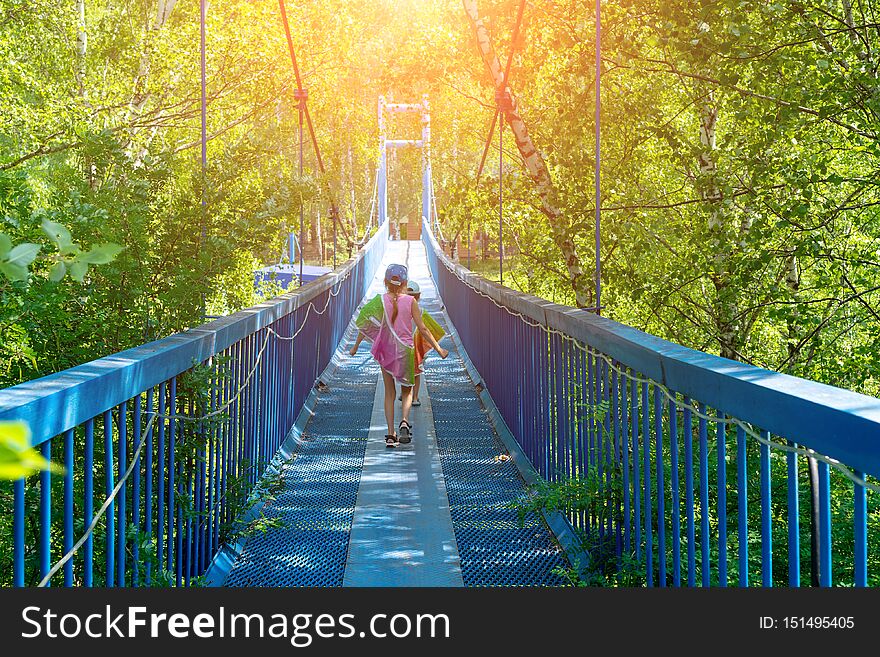 Two little happy girls walk along a hanging bridge on a sunny day.