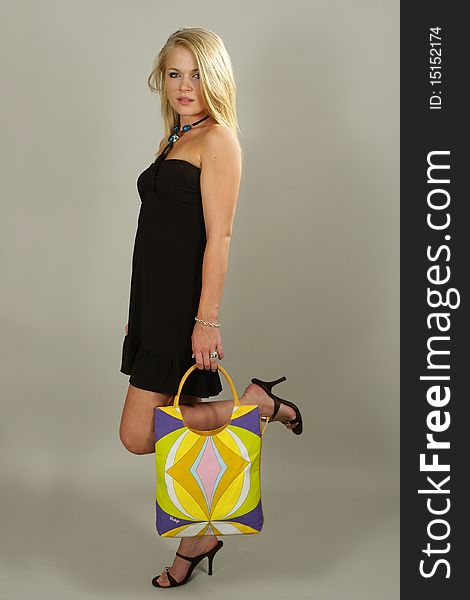 Beautiful blonde young girl in a black dress walking with a hand bag. Beautiful blonde young girl in a black dress walking with a hand bag