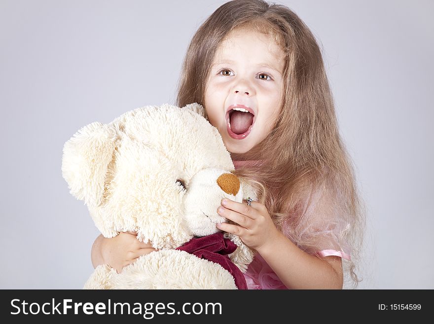 Little shouting girl embraces bear cub. Studio shot.