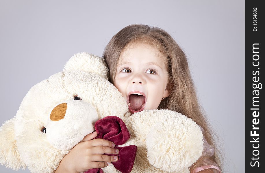 Little shouting girl embraces bear cub. Studio shot.