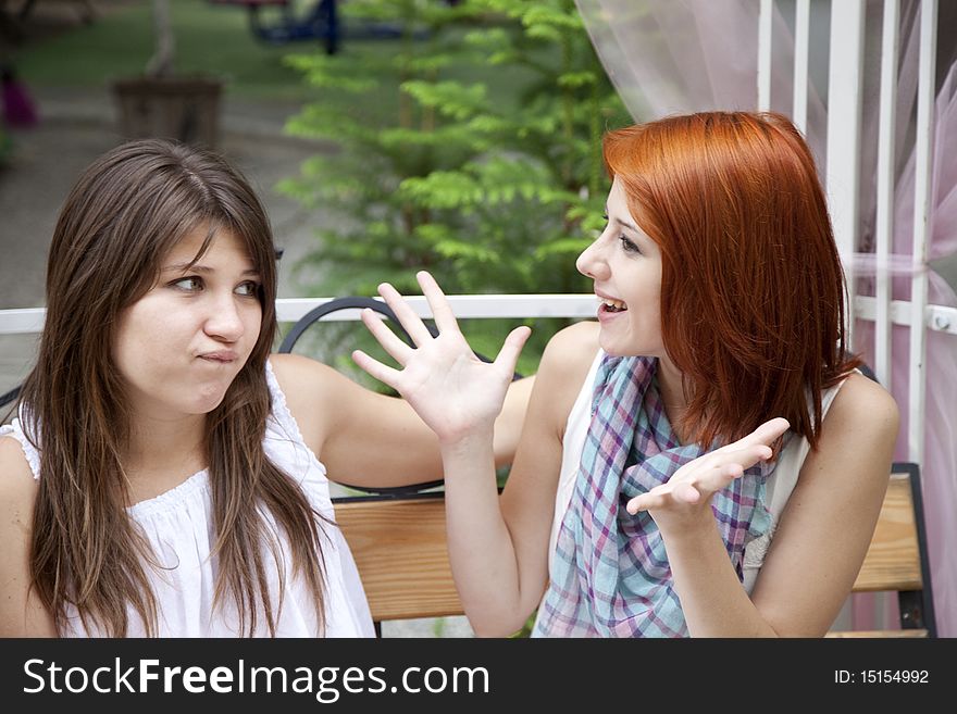 Two girls gossiping on bench at garden. Outdoor photo.
