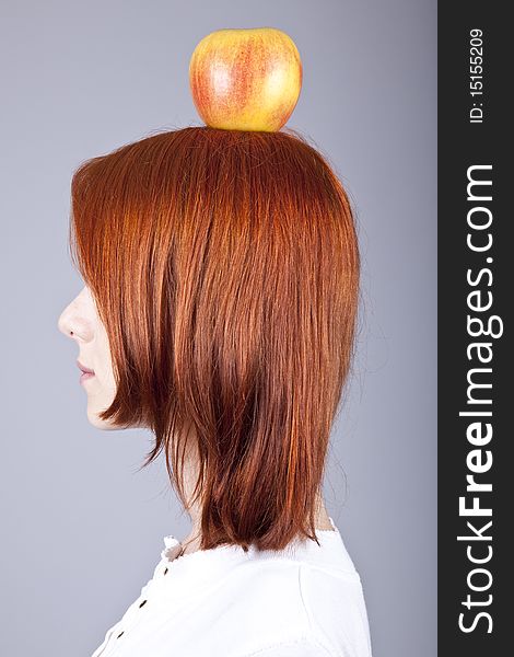 Red-haired girl keep apple on her head. Shot from sideview.