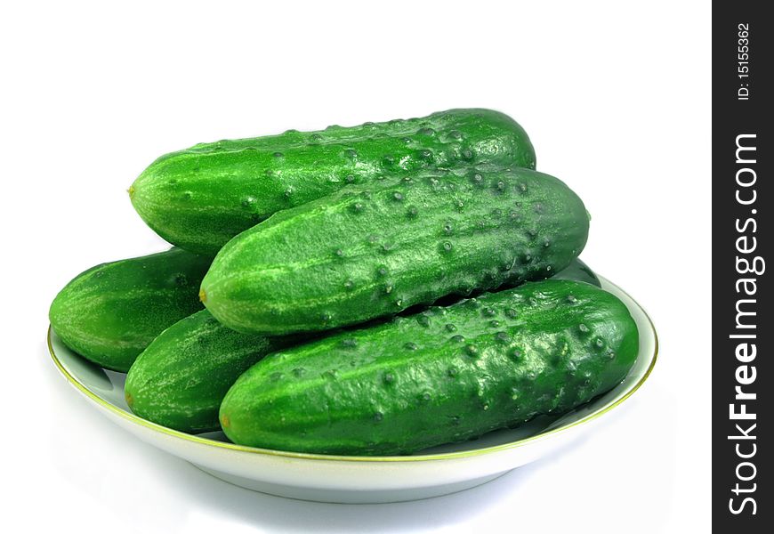 Five bright green cucumbers on a porcelain dish and vegetables on white background. Five bright green cucumbers on a porcelain dish and vegetables on white background