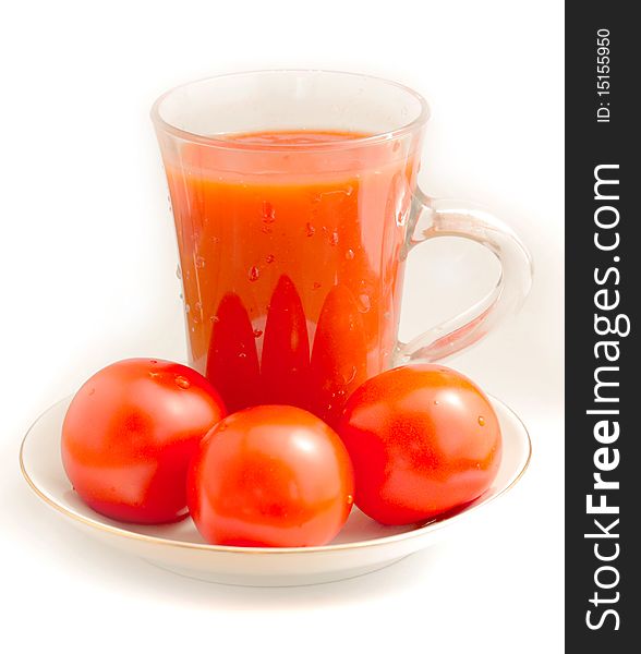 Tomato juice in a clear glass beaker, three ripe red tomatoes on a porcelain dish. Tomato juice in a clear glass beaker, three ripe red tomatoes on a porcelain dish