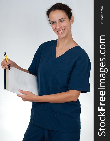 Brunette woman wearing blue scrubs against white background, holding tablet of paper and yellow pen. Brunette woman wearing blue scrubs against white background, holding tablet of paper and yellow pen