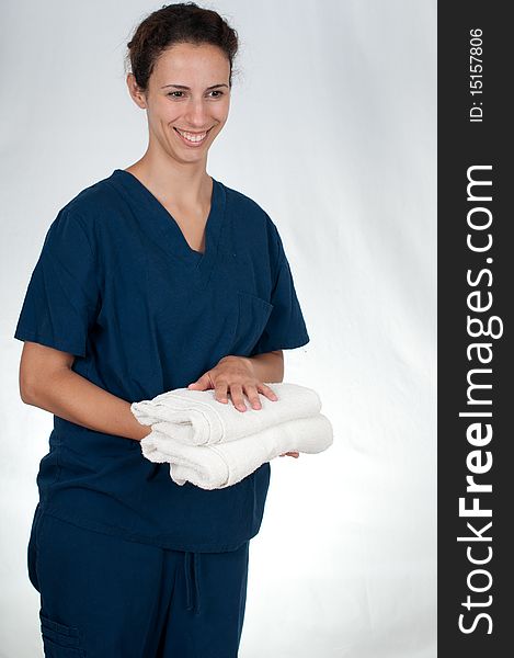 Brunette woman wearing blue scrubs against white background, holding two folded white towels. Brunette woman wearing blue scrubs against white background, holding two folded white towels