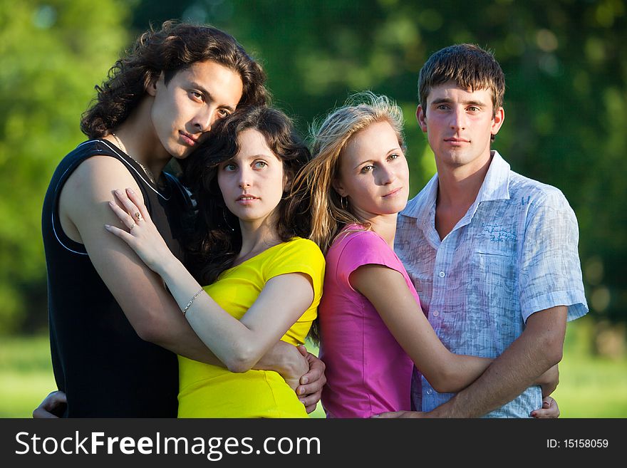 Four young people embrace and stand in the park and look forward