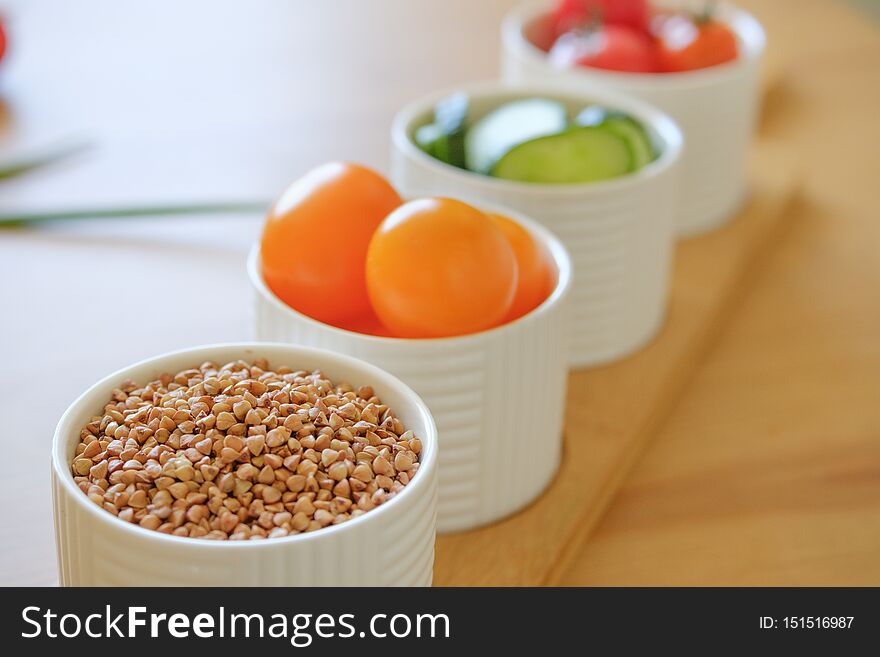 Yellow and red cherry tomatoes sliced cucumbers and buckwheat lie in white ceramic bowls. Yellow and red cherry tomatoes sliced cucumbers and buckwheat lie in white ceramic bowls