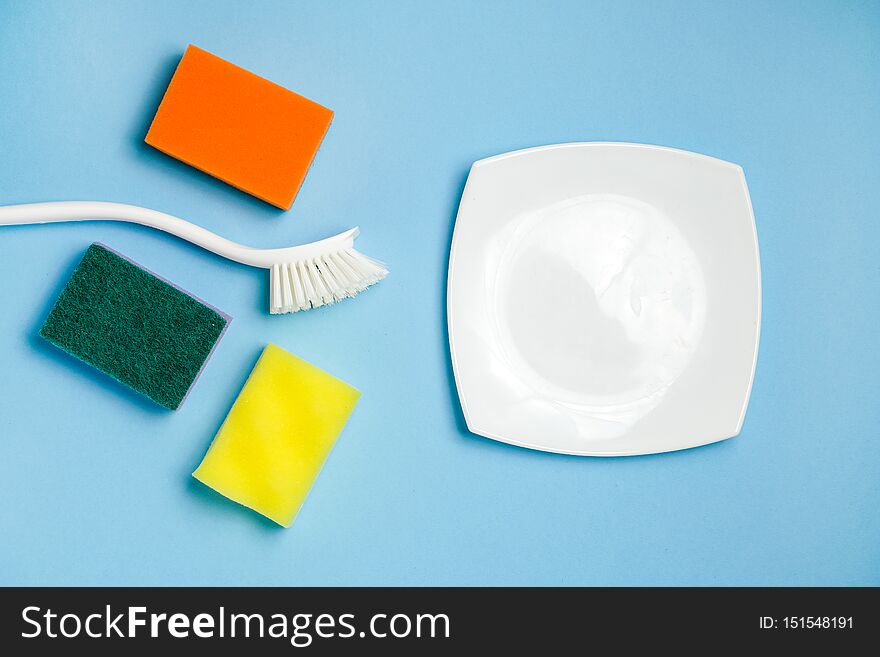 White glass plate, foam sponges and plastic brush for washing dishes. Cleaning accessories