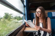 Pretty Young Woman In A Stylish Striped Summer Dress In Glasses Sits In The Train Near The Window And Reads An Interesting Book. Stock Photos