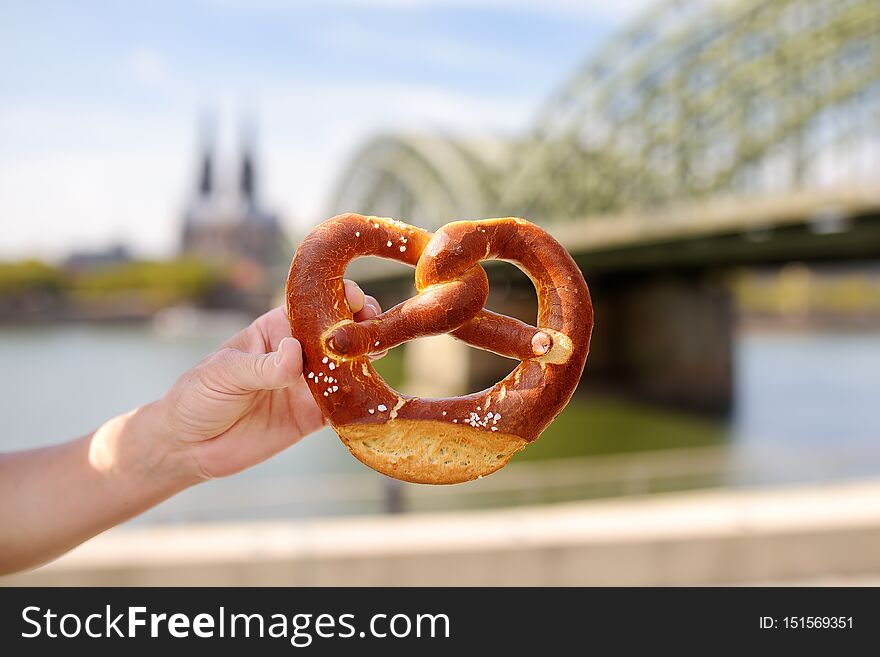 Traditional germany food pretzel on background of embankment of Rhine and Cologne Cathedral, Hohenzollern Bridge in Koel, Germany