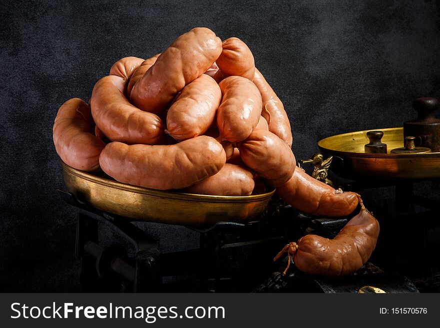 big bunch of raw short thick wieners with natural casings rolled in spiral on antiquarian scales over black background. big bunch of raw short thick wieners with natural casings rolled in spiral on antiquarian scales over black background