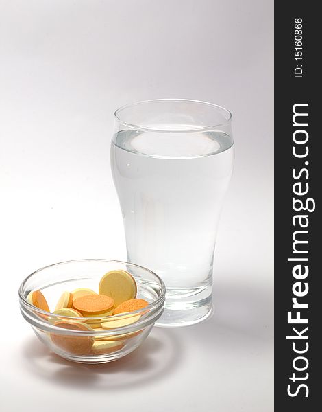 A glass of water and a bowl of effervescent vitamine tablets. A glass of water and a bowl of effervescent vitamine tablets