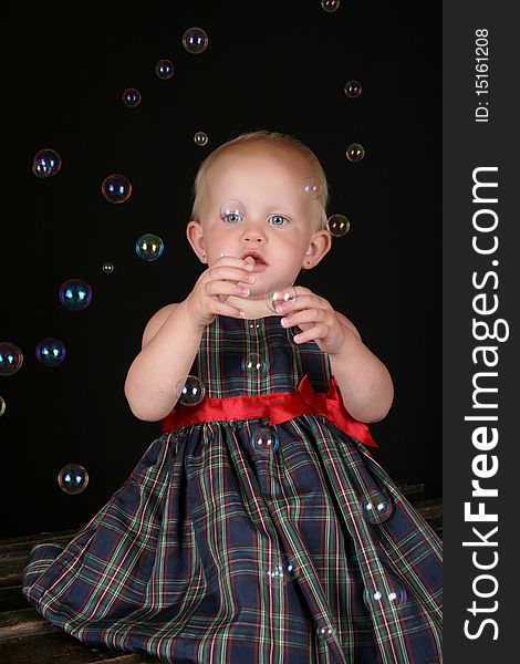 Cute blond toddler girl surrounded by bubbles sitting on a wooden trunk. Cute blond toddler girl surrounded by bubbles sitting on a wooden trunk