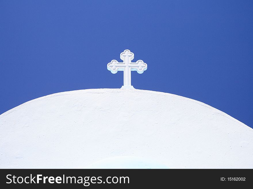 White cross on small greek church under blue sky