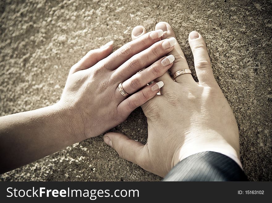 Hands of the newly-weds, on textured surface. Color-processed