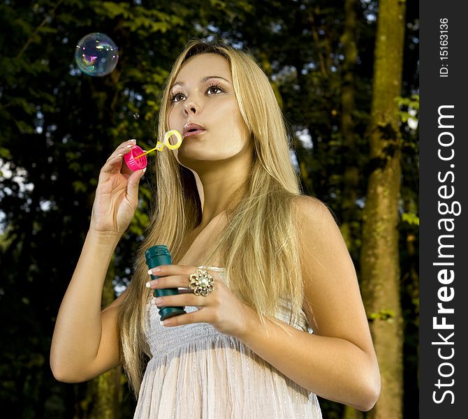 Blonde young woman blowing soap bubbles in summer day. Blonde young woman blowing soap bubbles in summer day