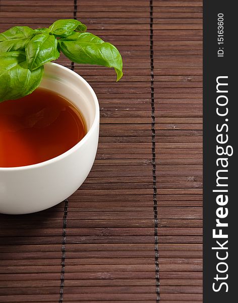 Cup of tea with basil leaves on a bamboo mat. Cup of tea with basil leaves on a bamboo mat