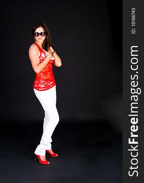 Photo of standing girl in a red blouse and in sunglasses on black background. Photo of standing girl in a red blouse and in sunglasses on black background