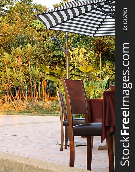 Picture of garden table and chairs with striped umbrella set infront of beautiful natural garden. Picture of garden table and chairs with striped umbrella set infront of beautiful natural garden.