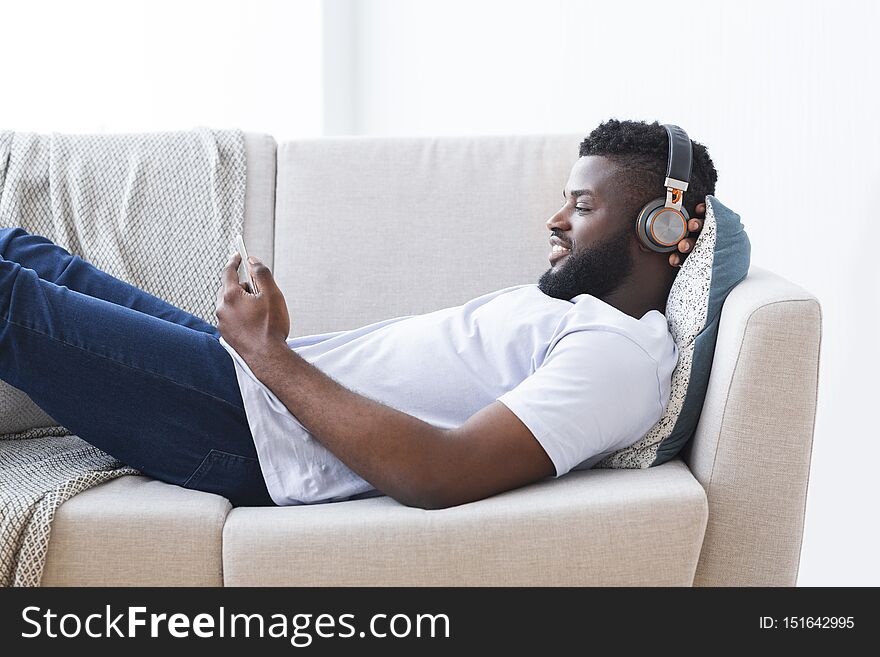Relax for millennial men. African guy watching videos on smartphone, using mobile application, empty space