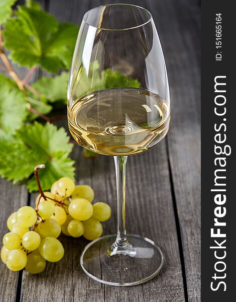 White wine in a glass and a bunch of grapes on an old wooden table
