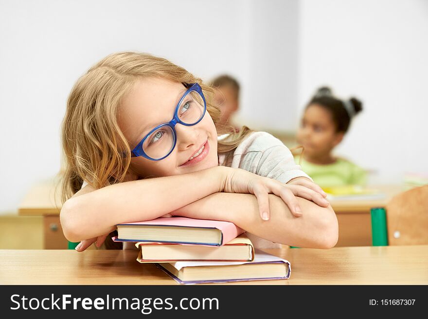 Girl In Classroom At Desk Leaning Head On Books.