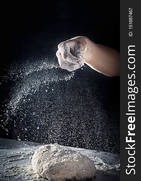 Chef prepares the dough with flour. male sprinkling flour over dough on table on dark background. Vertical. Copy space. Conceptn of flying food. Gluten free dough for pasta, bakery or pizza
