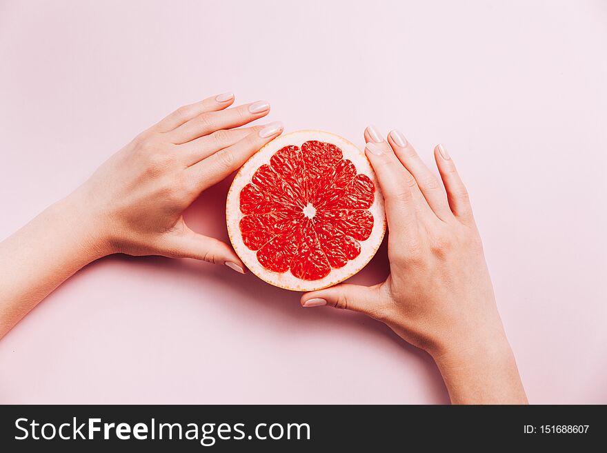 Female`s hands holding grapefruit on pink background with tropic plants and leaves