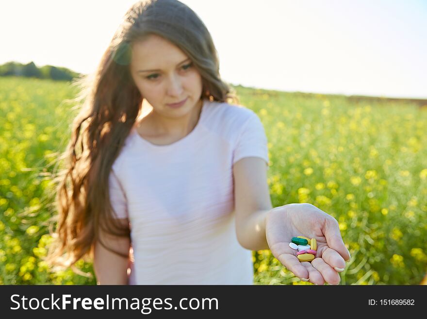 The girl pulls a hand holding a many of pills in the palm. In a yellow flowered field