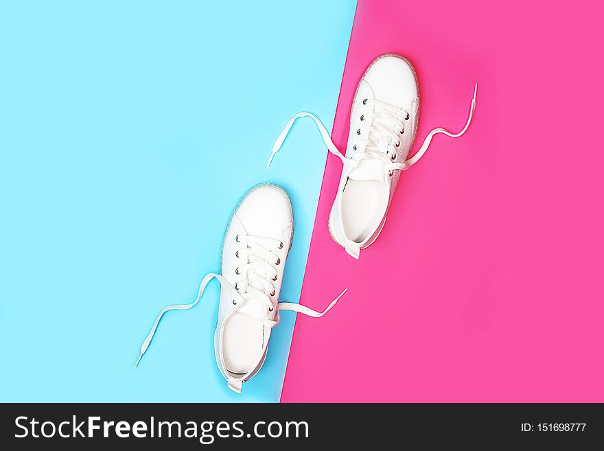 White sneakers are lying on bright neon color blue pink background. Top view. Flat lay. Copy space. Black Friday, party, sport concept, outfit.